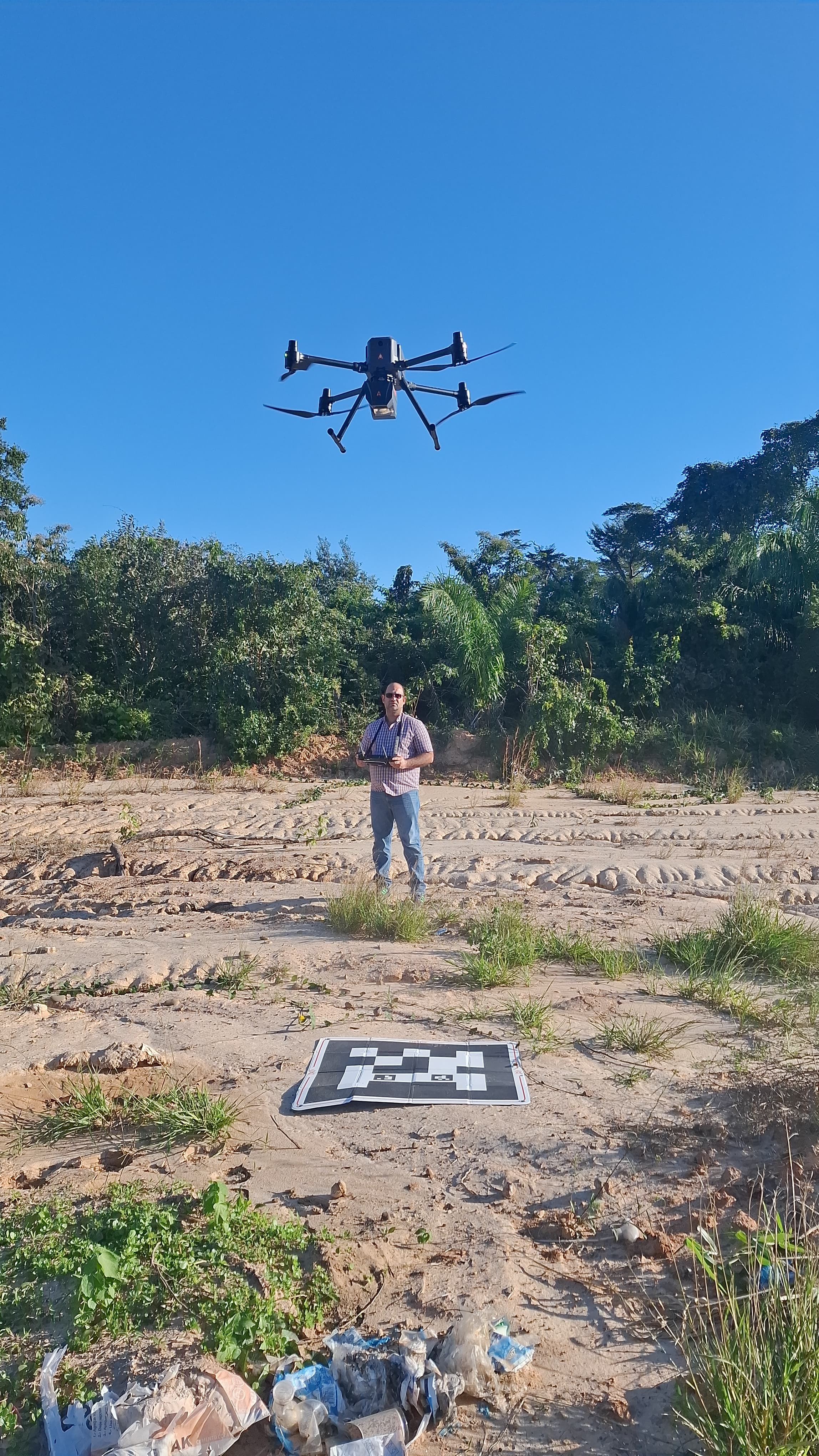 Dron CHCNAV X500 con sensor LiDAR AA6D de doble cámara en vuelo durante un levantamiento topográfico en Santa Cruz, Bolivia, con el operador en tierra junto al helipuerto portátil
